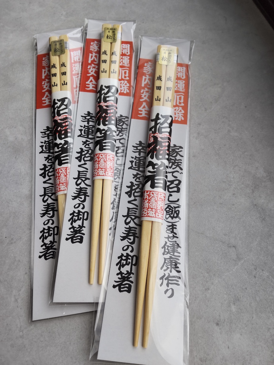 Three pairs of packaged wooden chopsticks from Naritasan Temple on a gray surface
