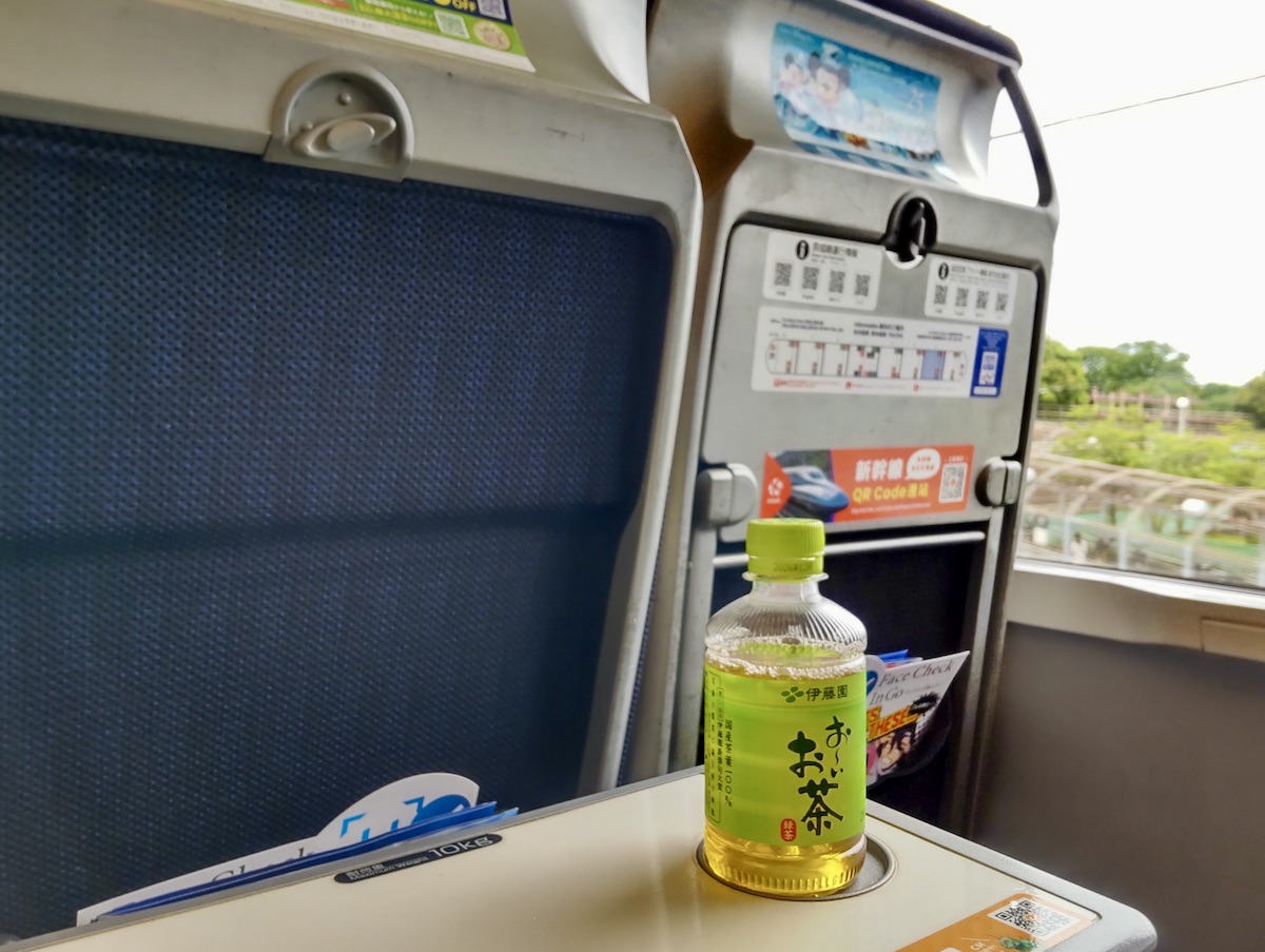 A bottle of Japanese green tea rests on a tray table inside a train