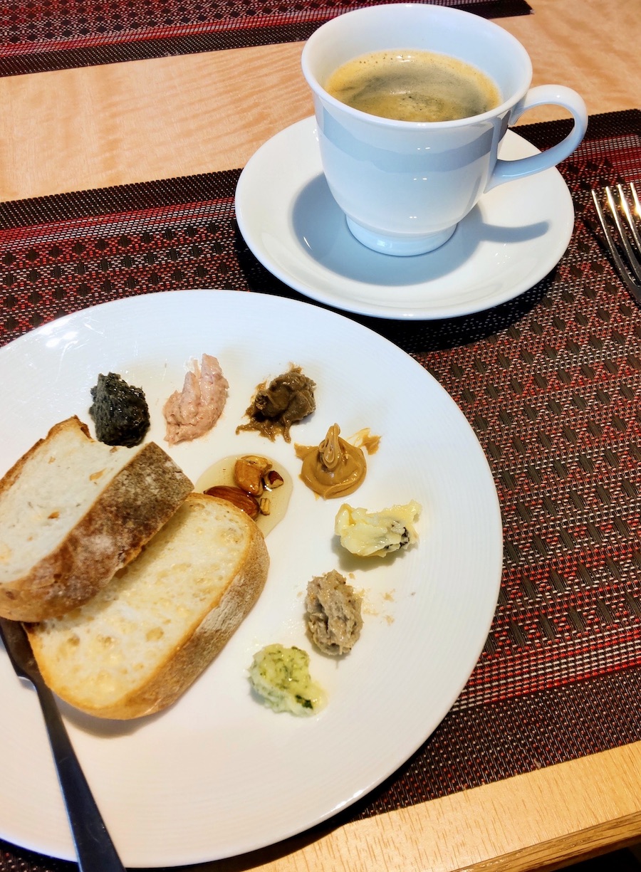 A breakfast plate with sliced bread, various spreads, and a cup of coffee
