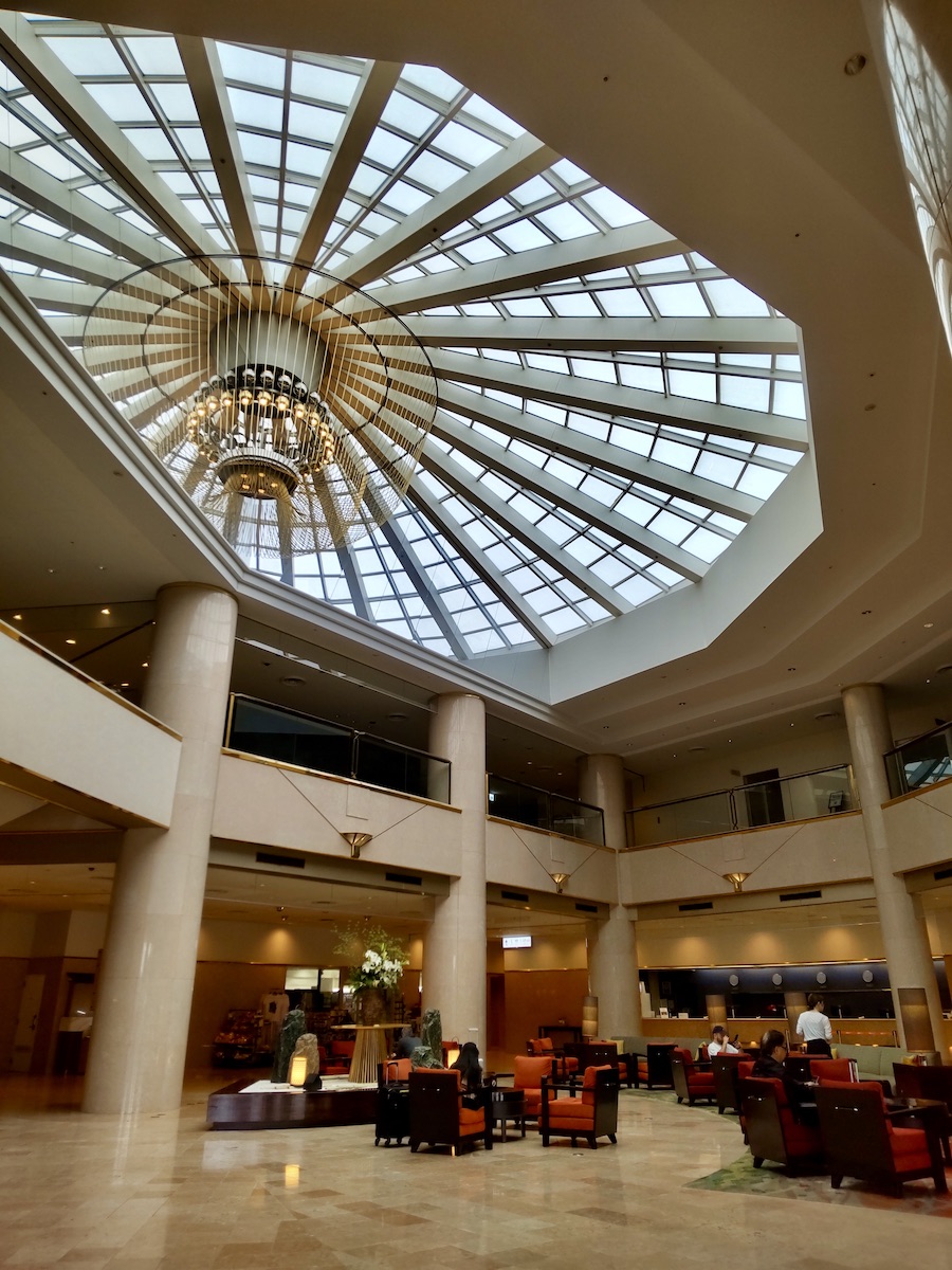 A spacious hotel lobby atrium featuring a skylight roof and comfortable seating areas