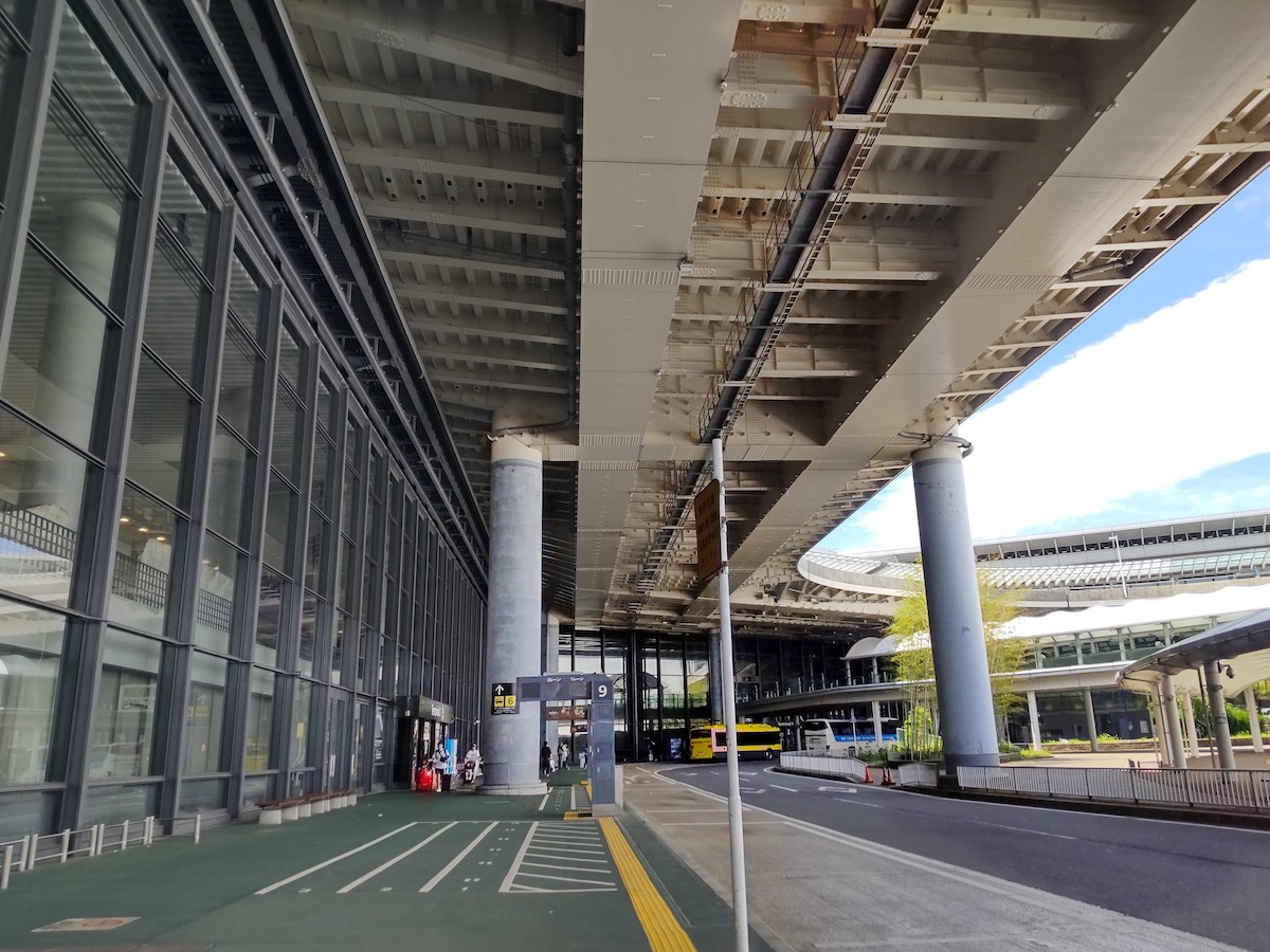 A spacious outdoor bus pickup area at the airport terminal under a large overpass