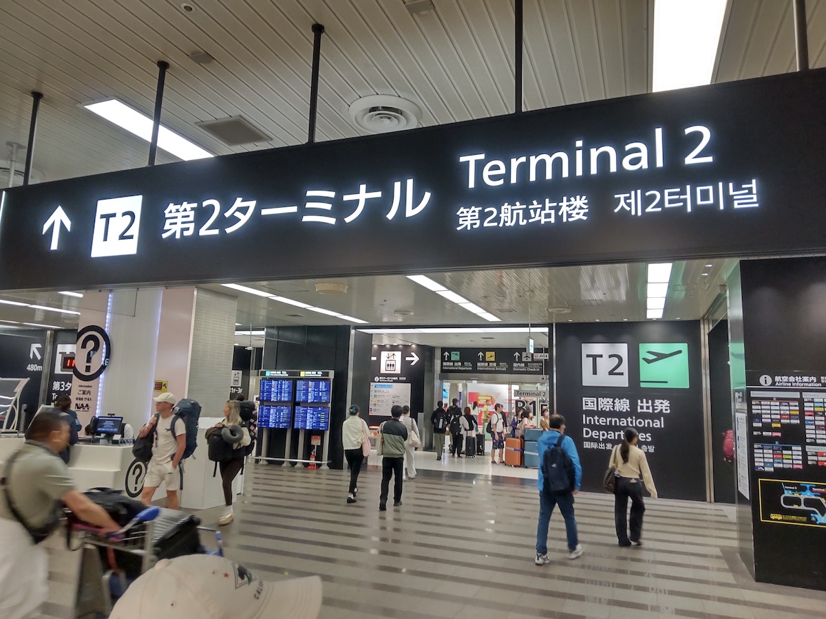 Travelers walk with luggage underneath a prominent Terminal 2 sign in an airport
