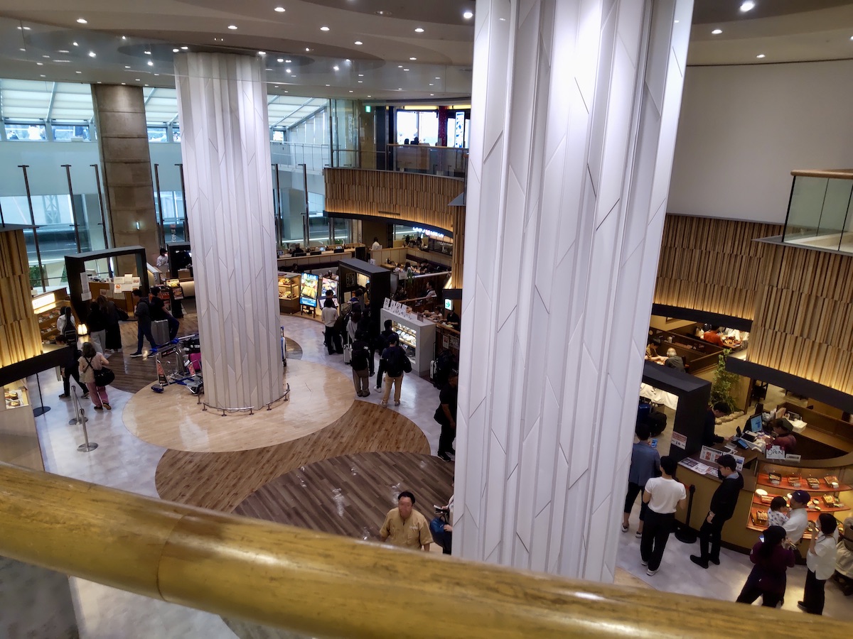 A spacious airport indoor plaza featuring high white pillars and various dining shops