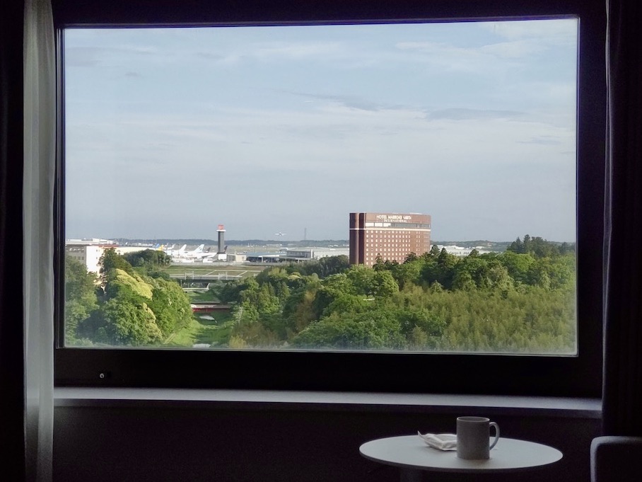 A scenic view of an airport runway, control tower, and trees framed by a large hotel window