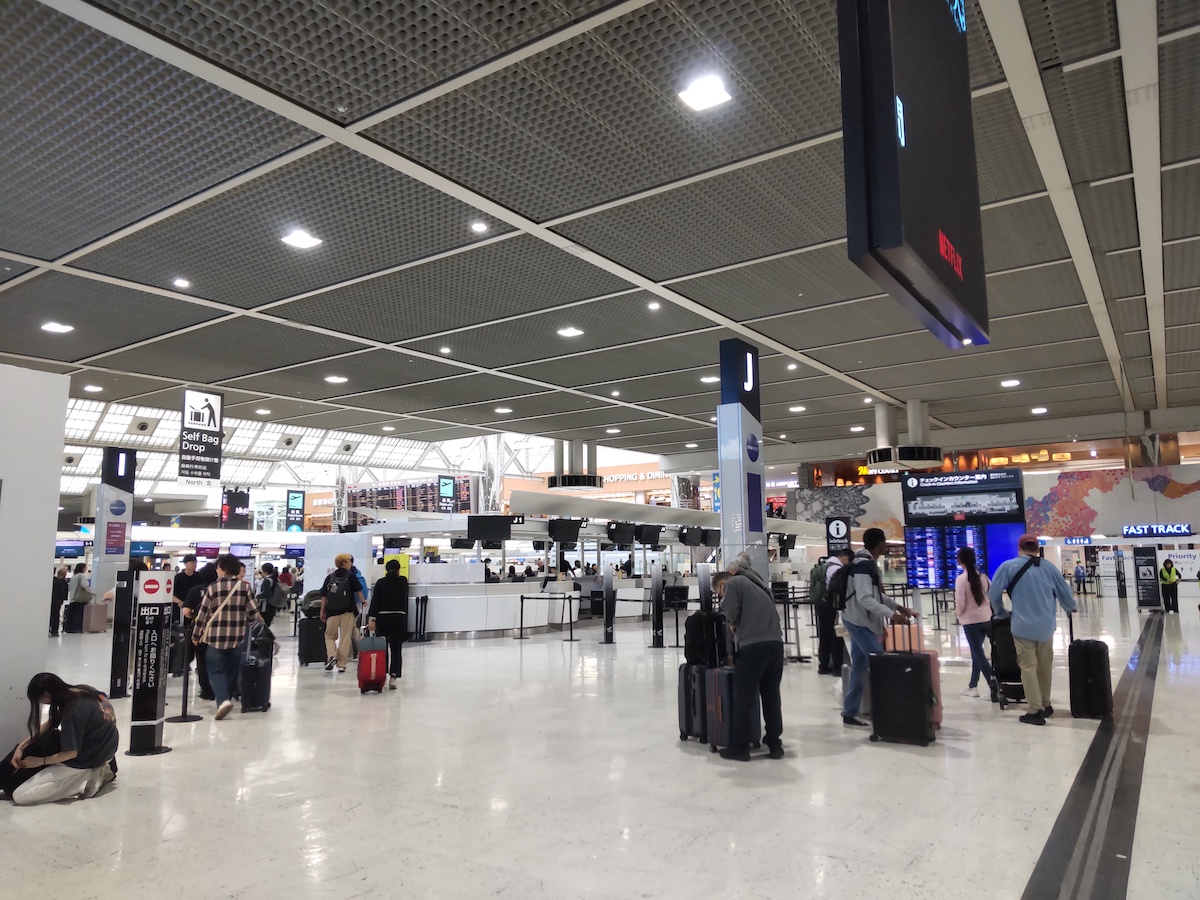 Travelers with luggage navigate a spacious airport check-in terminal with digital displays
