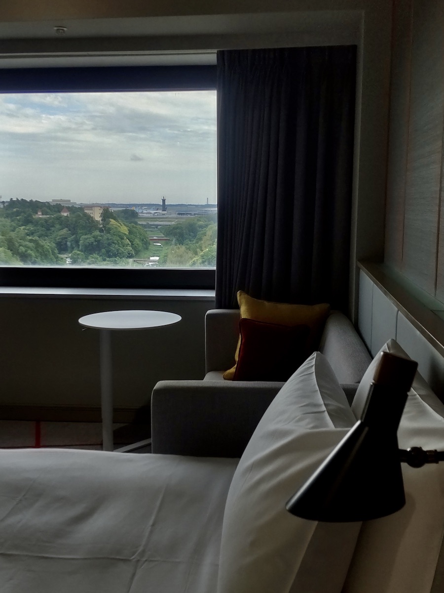 A modern hotel room with a window view of an airport runway and surrounding trees