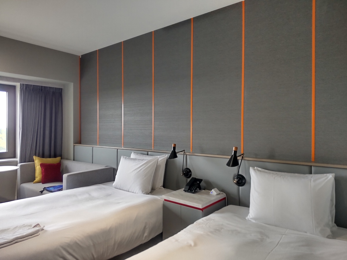 A modern hotel twin room featuring grey textured walls with stylish orange vertical stripes