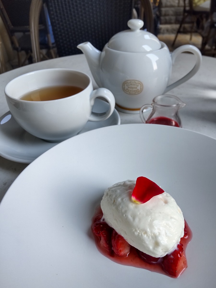A delicious white dessert topped with a rose petal next to a teapot
