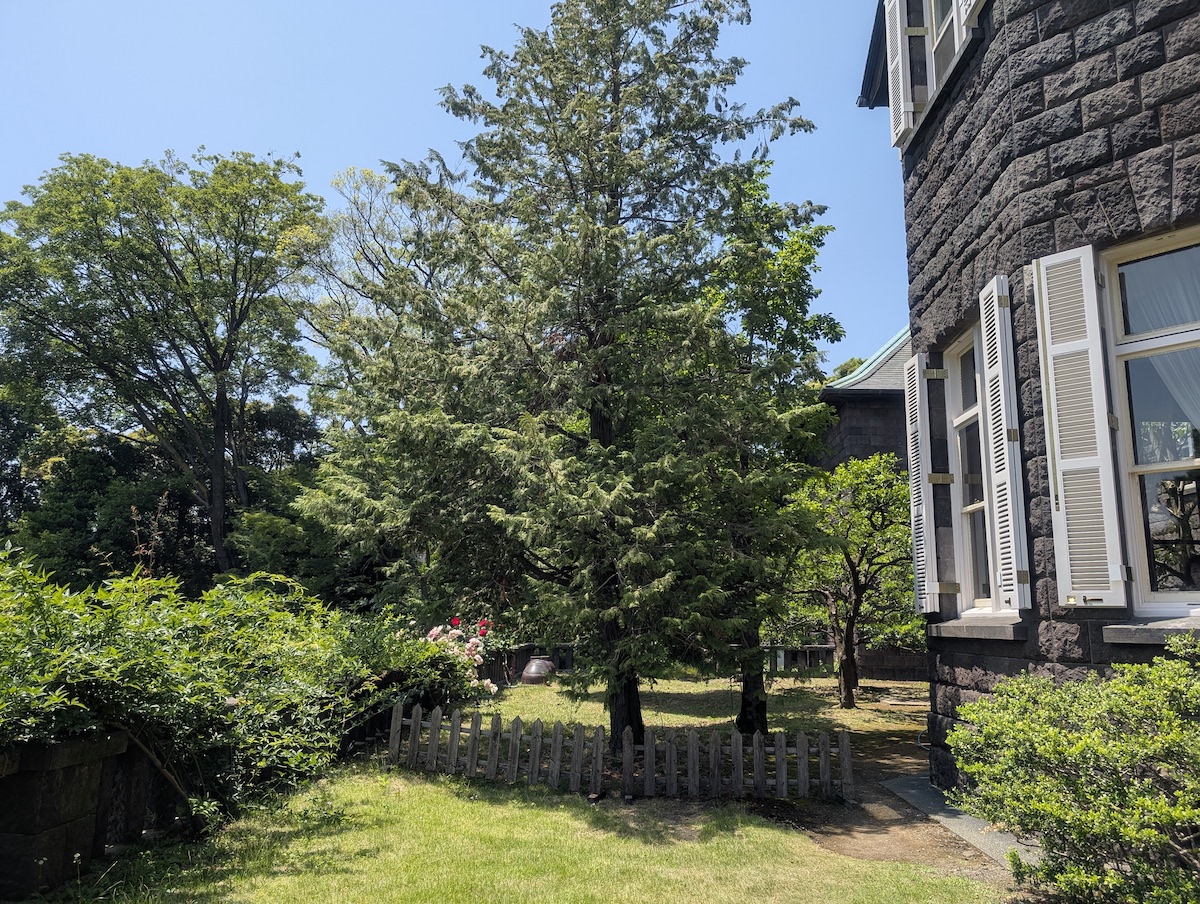 A historic stone mansion with white shutters next to a lush green garden