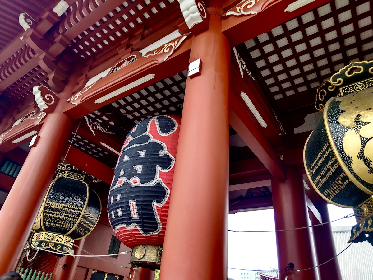 A large red lantern and ornate bronze lanterns hanging under a temple gate