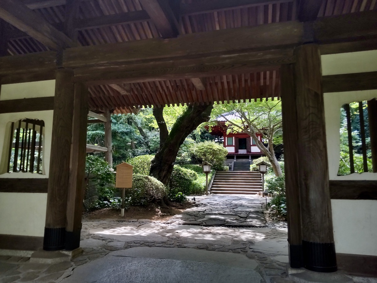 A view of a green garden and temple building framed by a wooden gate