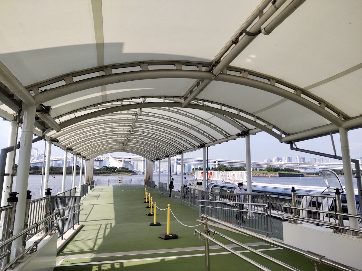 An arched covered pier with a modern water bus docked near Rainbow Bridge