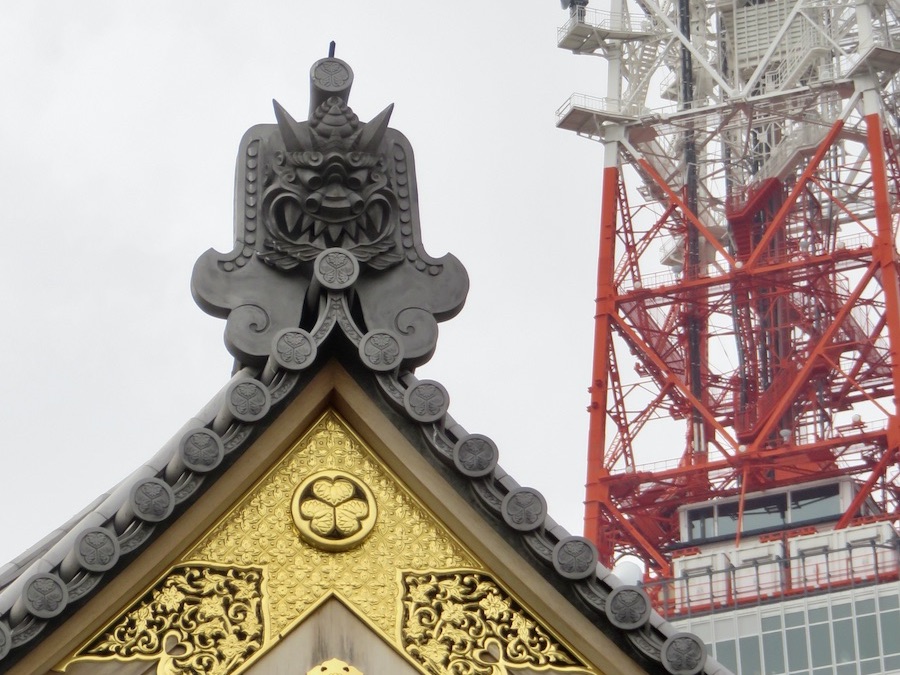 A ornate Japanese temple roof tile set against the red Tokyo Tower