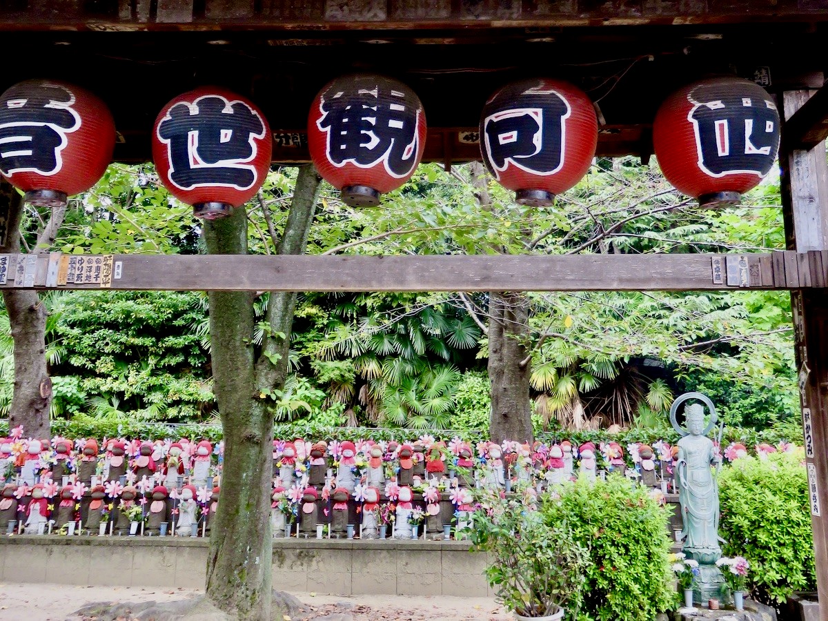 Rows of small stone Jizo statues with red caps behind wooden paper lanterns