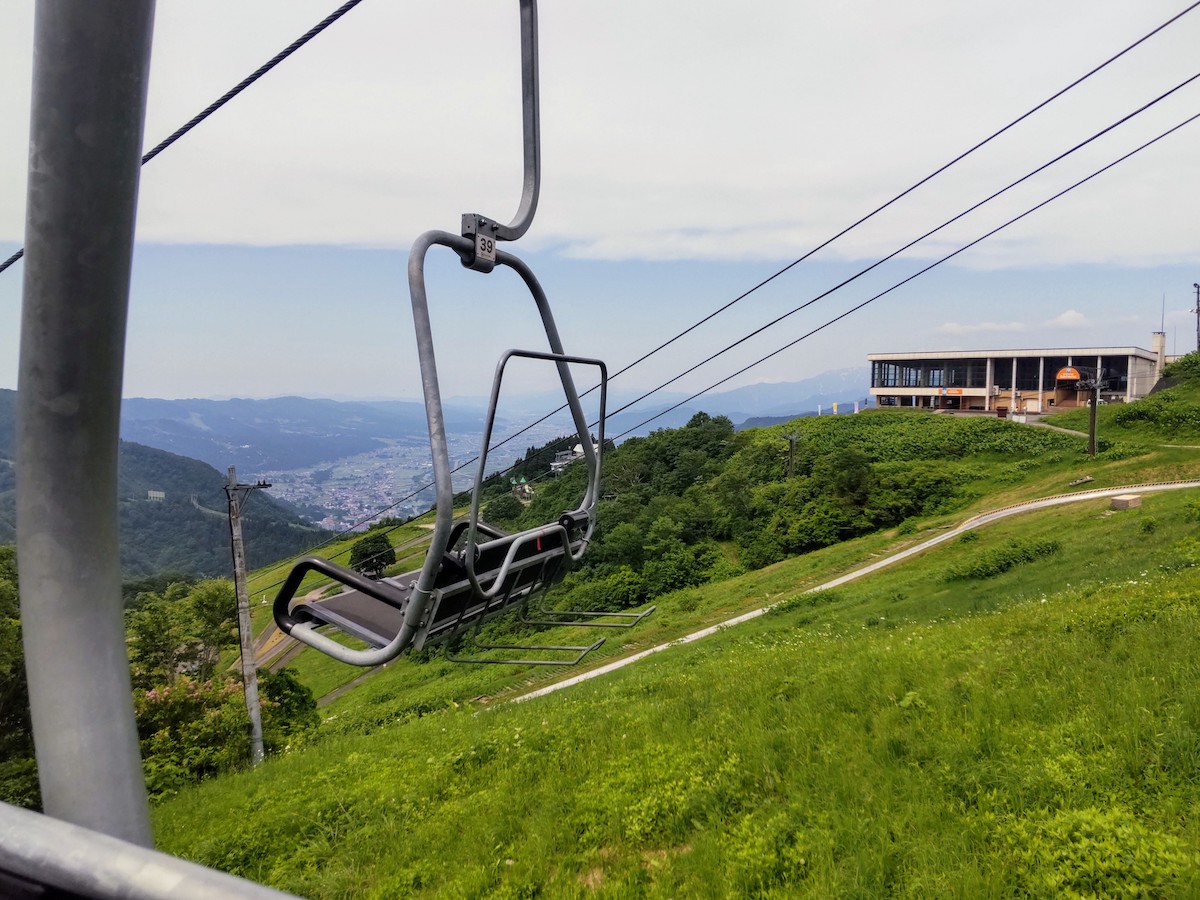 View from a lift rising over lush green hills toward mountain station