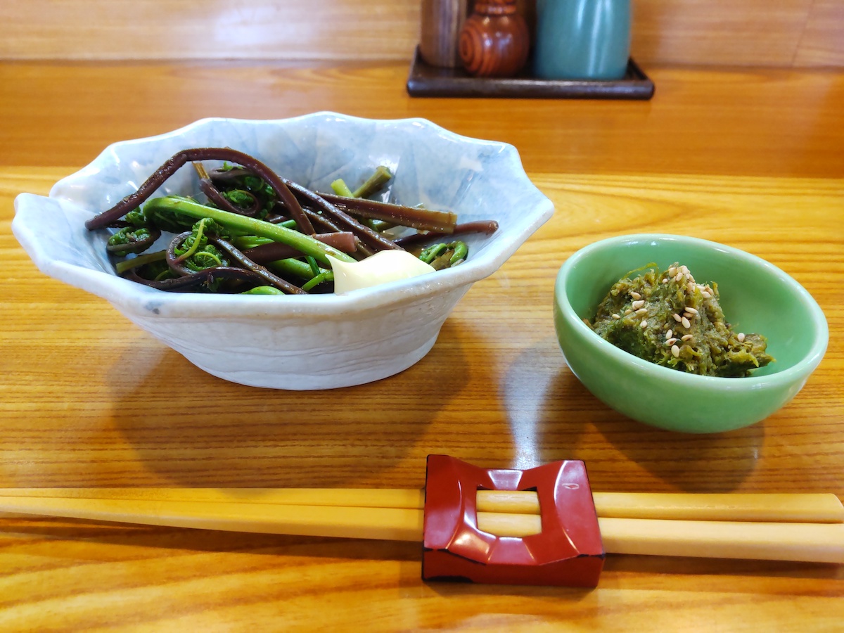 Small bowls of seasonal mountain vegetables served with chopsticks on wooden counter