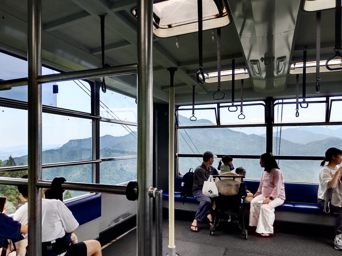 View inside a ropeway car with large windows overlooking green mountains