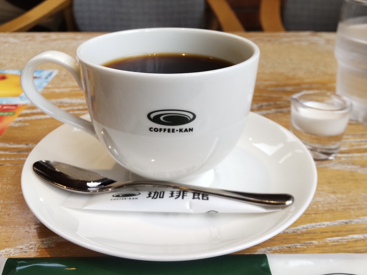 Freshly brewed black coffee in branded white cup with spoon and cream