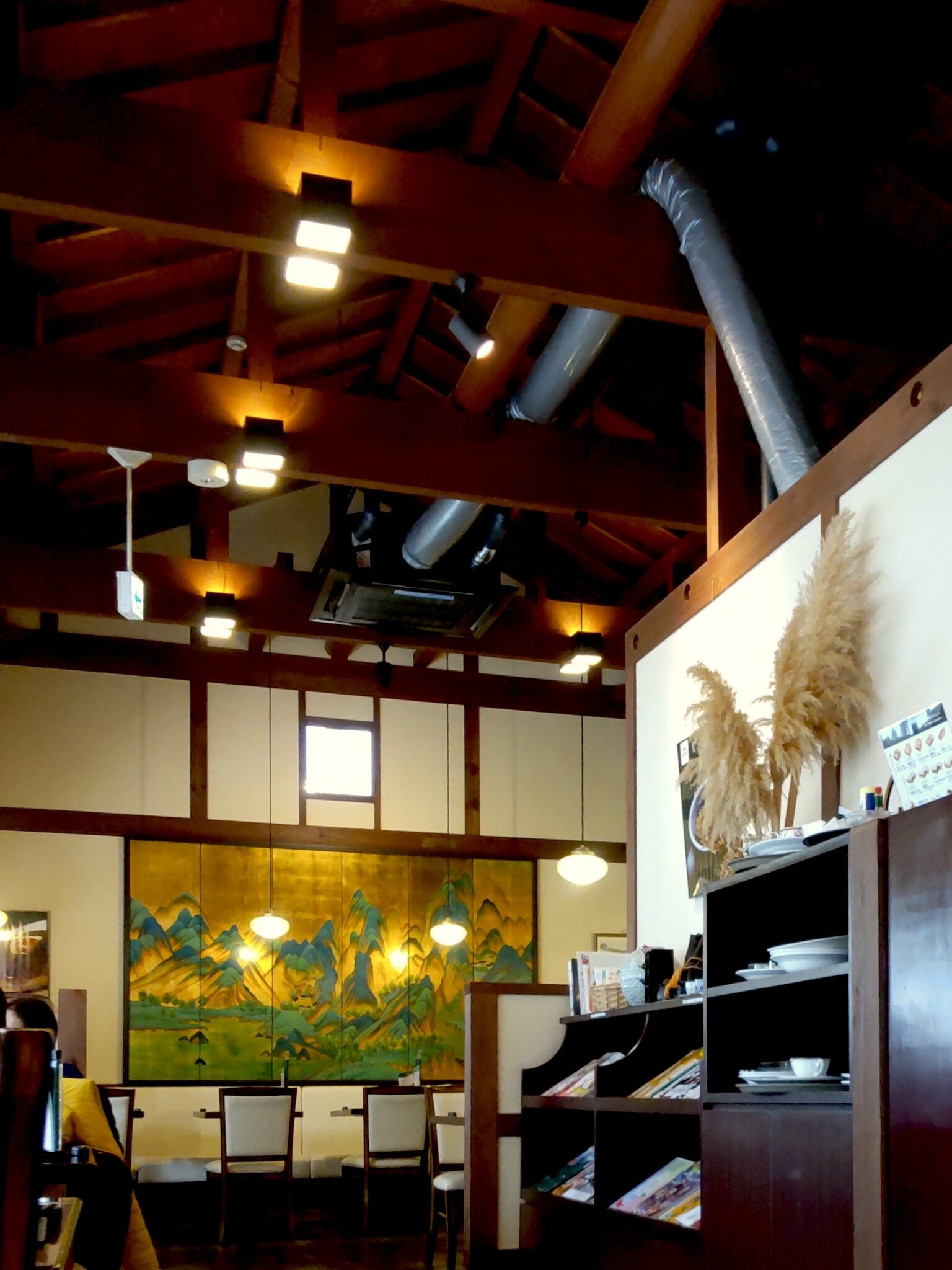 Cozy coffee shop with exposed wooden ceiling beams and golden landscape painting