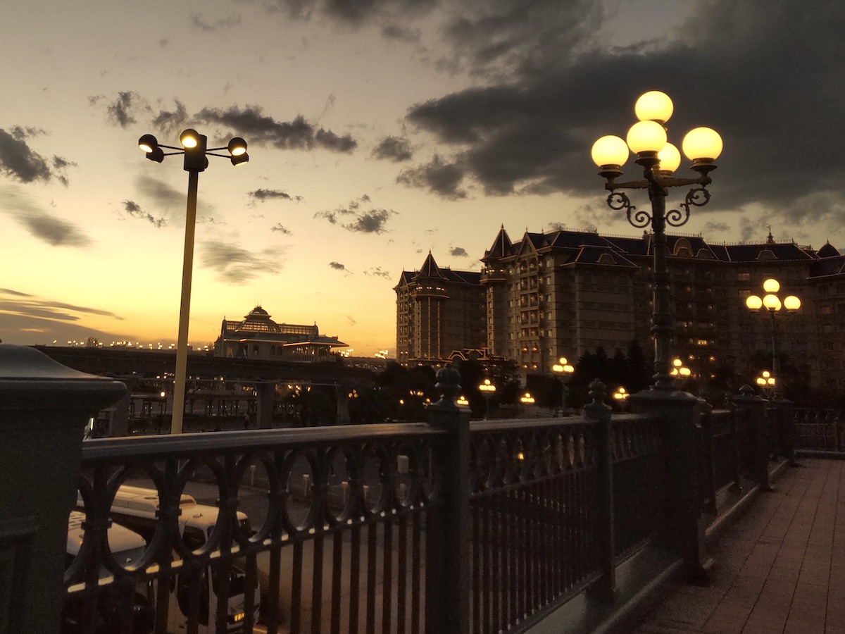 Illuminated street lamps along walkway with Tokyo Disneyland Hotel during sunset