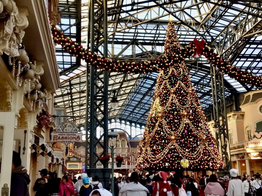 Sparkling Christmas tree towering over a crowded indoor theme park street