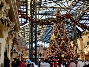 Sparkling Christmas tree towering over a crowded indoor theme park street