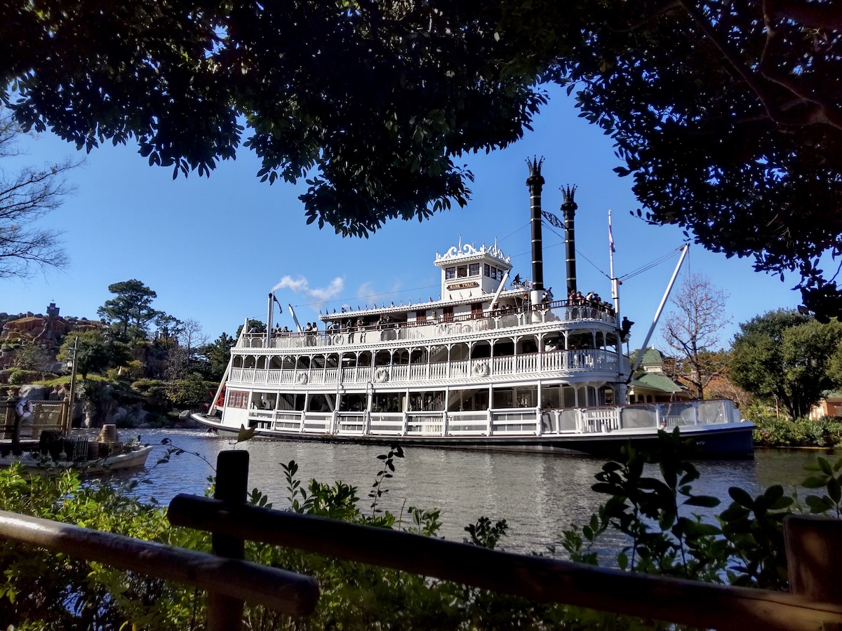 White riverboat Mark Twain cruising on a river framed by green trees